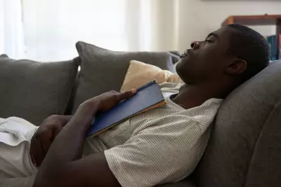 man napping on a couch with a book open on his chest