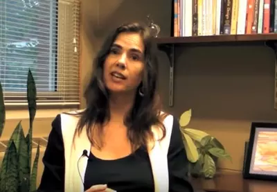kristin neff sitting in front of a bookshelf and looking into the camera